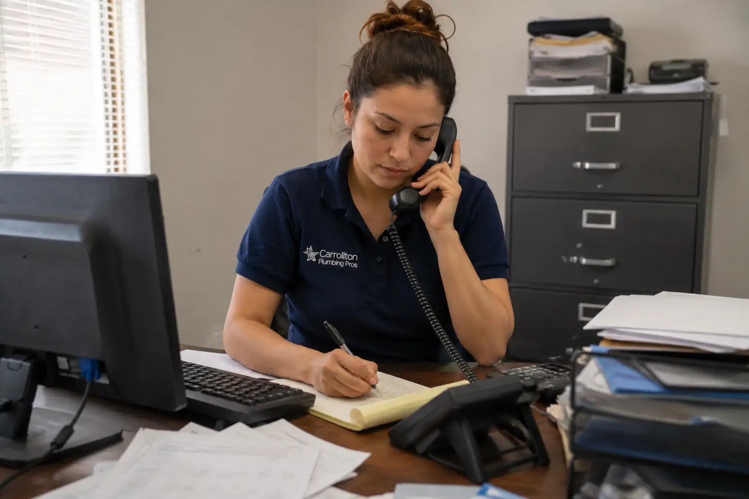 Carrollton Plumbing Pros dispatcher taking a service call at an office desk with a Carrollton, Texas service map behind