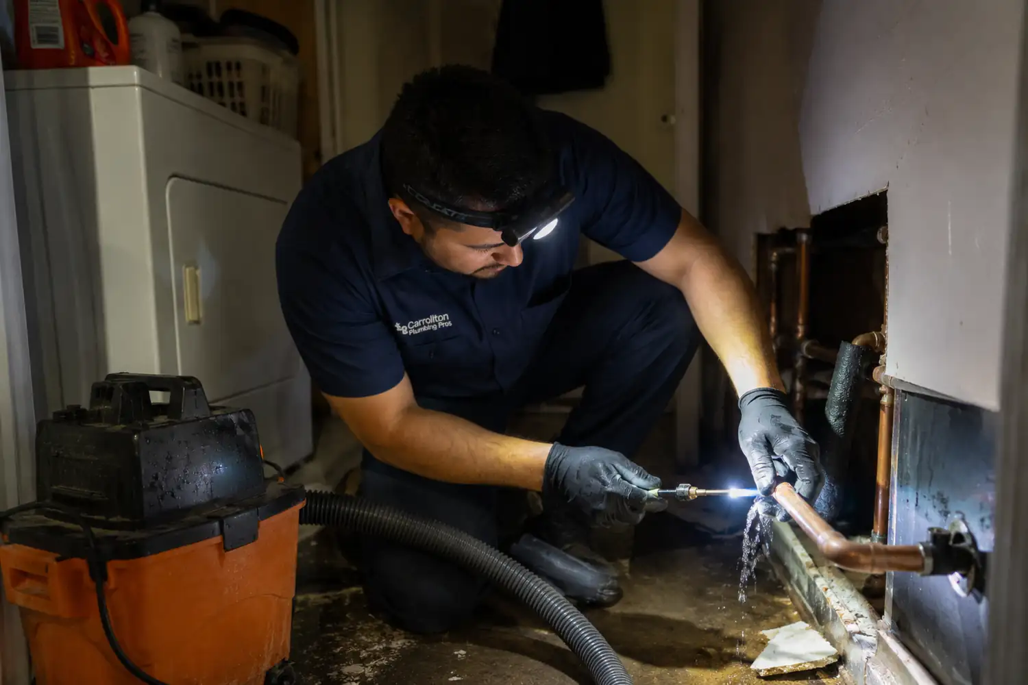 Emergency plumber Carrollton TX working a split copper supply line by headlamp in a flooded laundry room at night