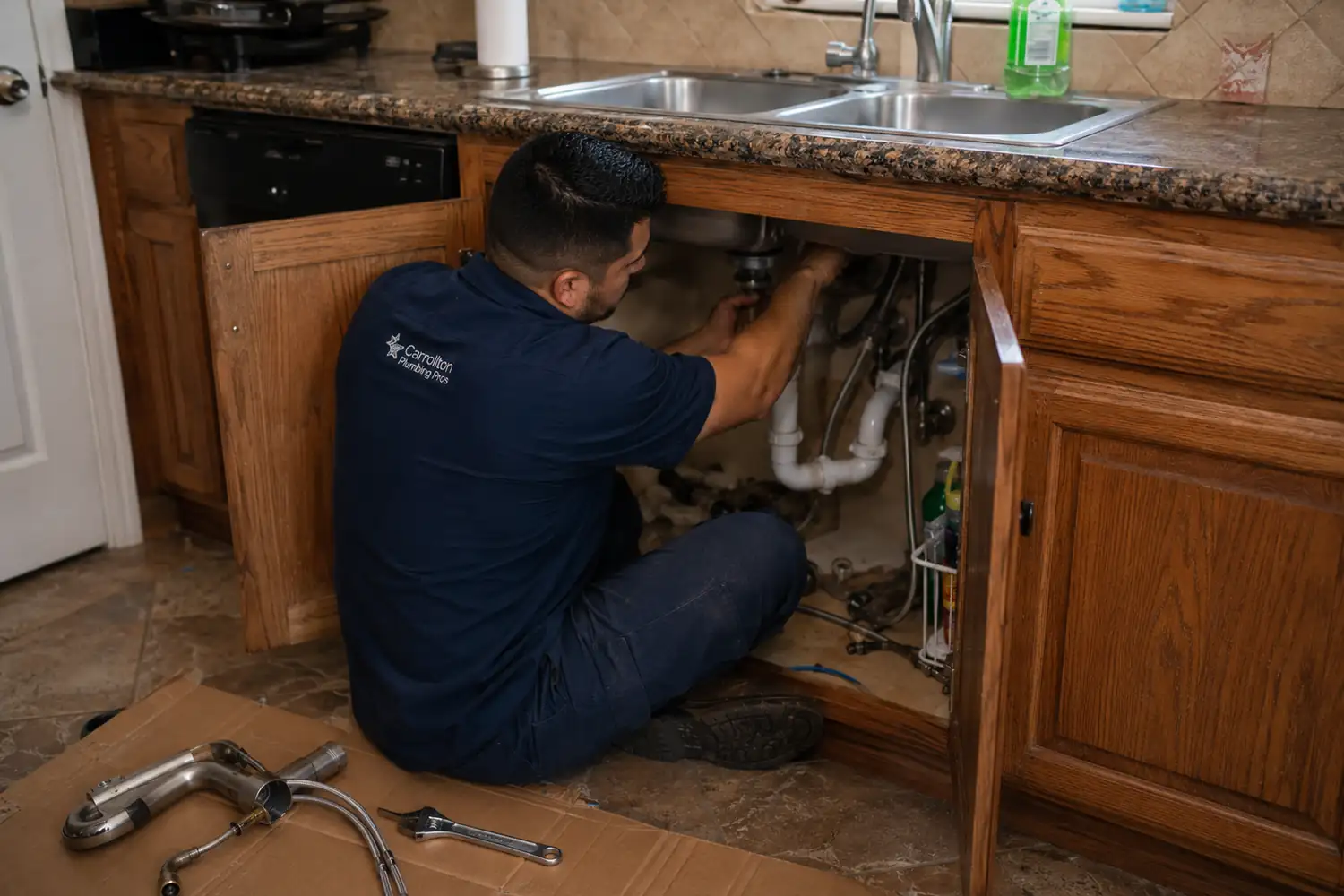 Faucet repair Carrollton TX technician tightening the mounting nut of a new pull-down kitchen faucet from inside the sink cabinet