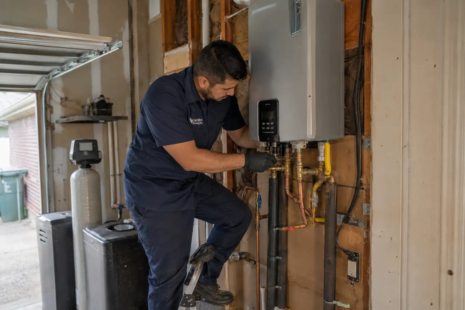 Tankless water heater installation Carrollton plumber connecting gas and water lines to a wall-mounted unit in a garage